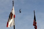 A Sheriff's Department helicopter flies between a California flag and an American flag